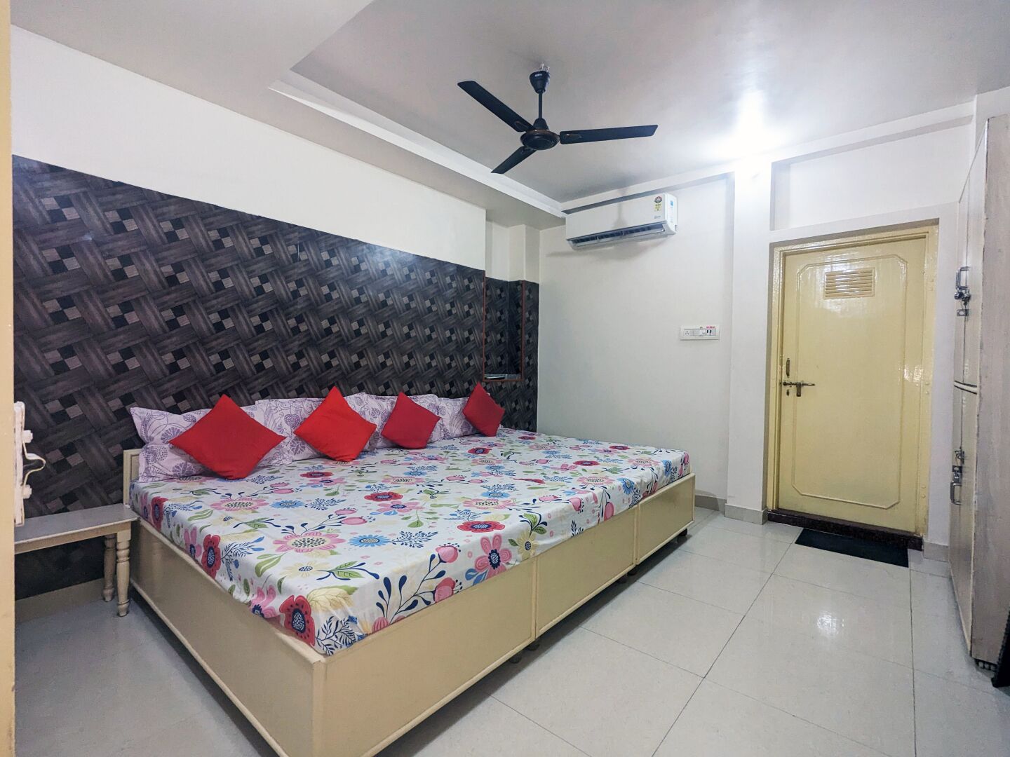 A bedroom with a bed, a ceiling fan, an air conditioner, and a door.