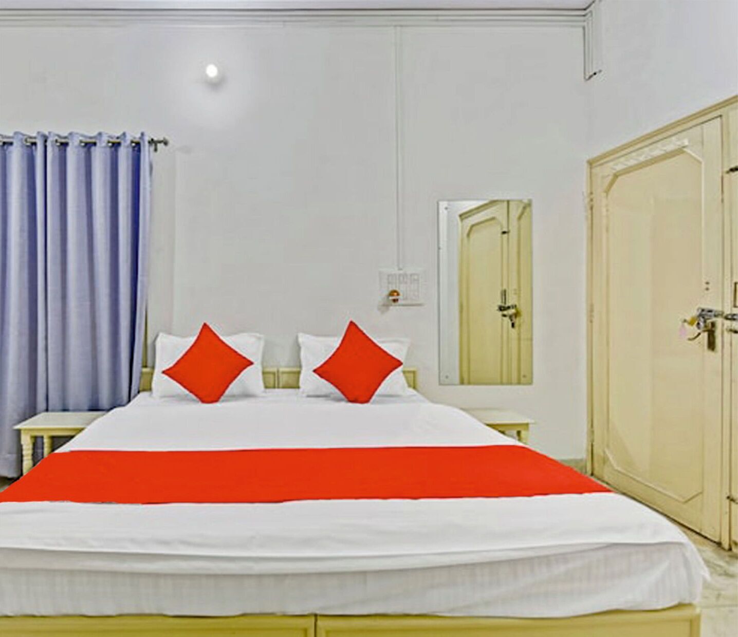 A hotel room with a bed, a nightstand, a mirror, and a wardrobe.