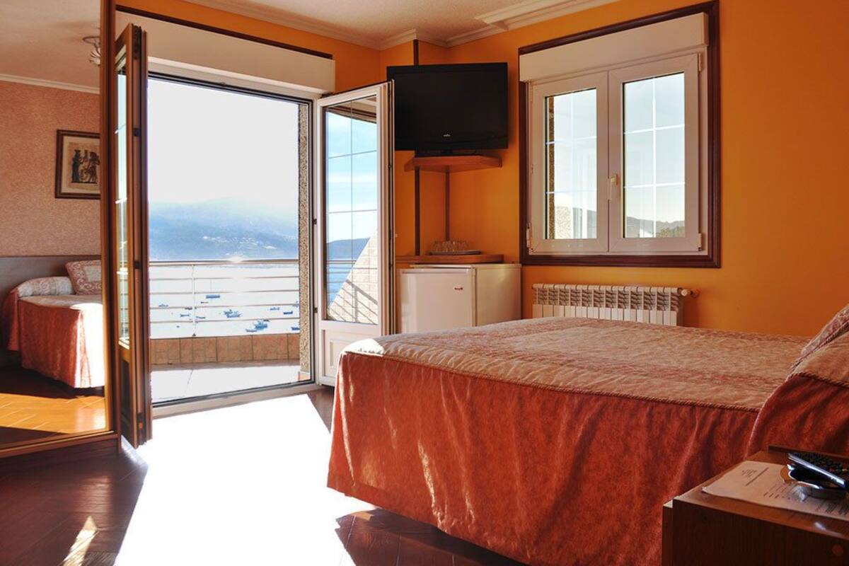 Habitación de hotel con cama, televisor, ventana con vistas y puerta que da a un balcón.