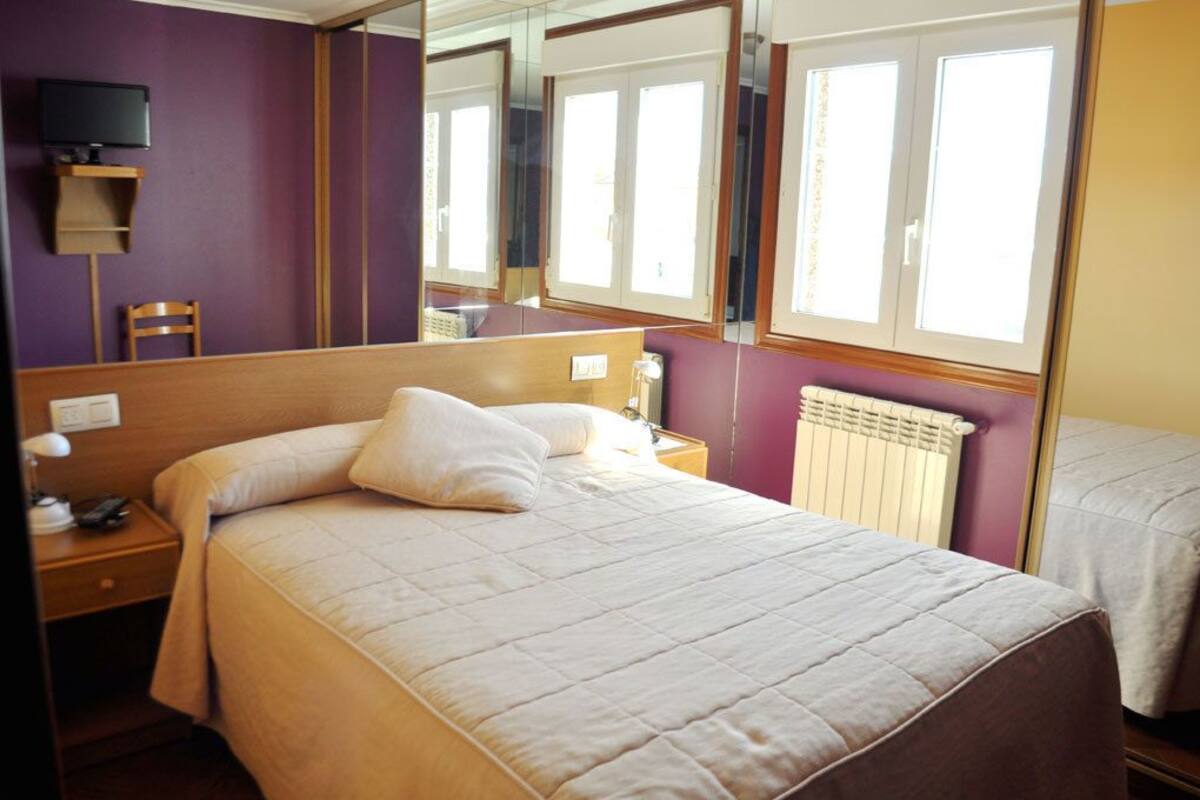 Habitación de hotel con cama, mesita de noche, lámpara y televisor sobre una estantería.
