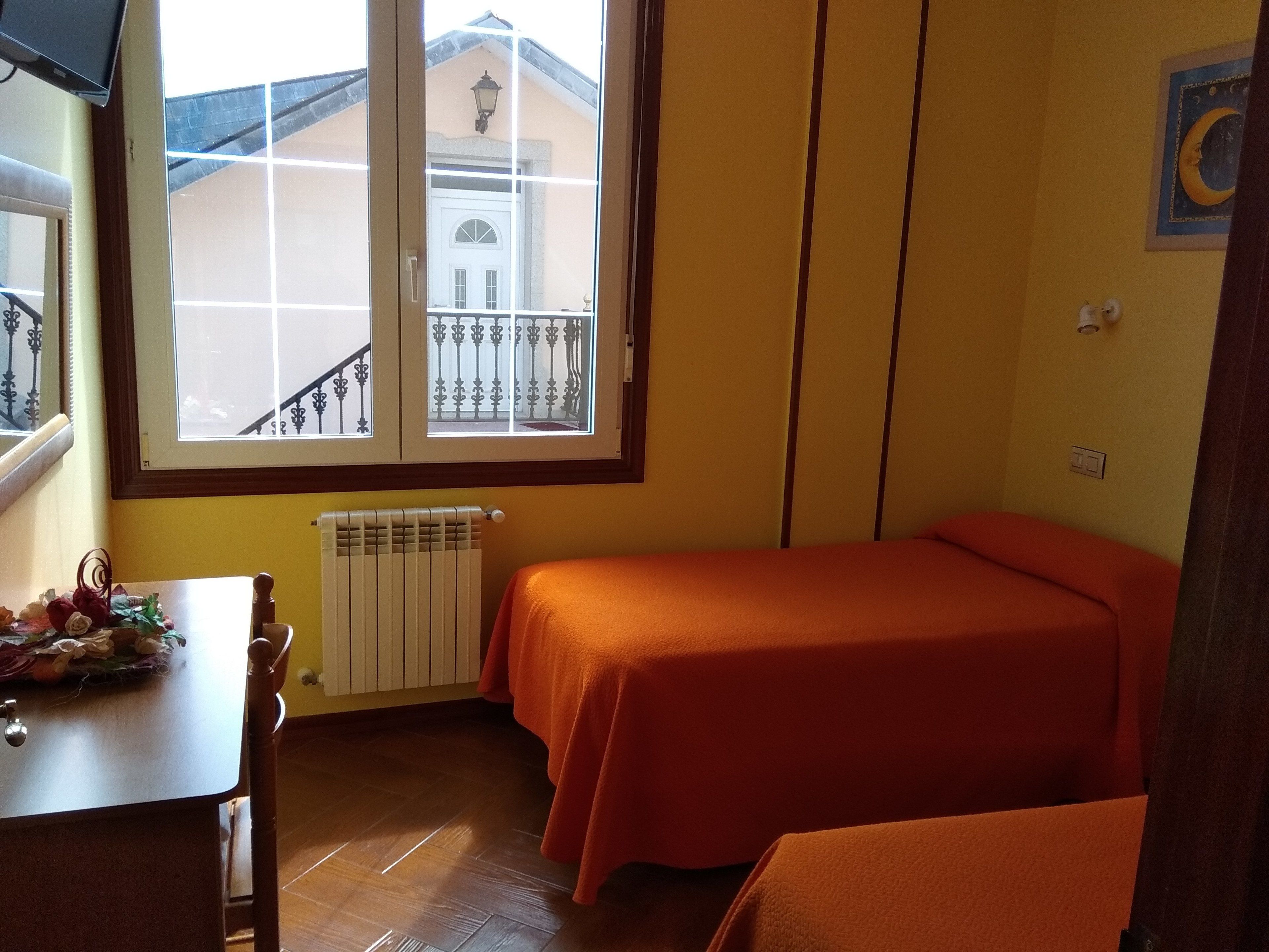 Habitació amb dos llits, un radiador, una finestra amb vista a un edifici, una taula amb flors i una paret amb un quadre de la lluna gegant.