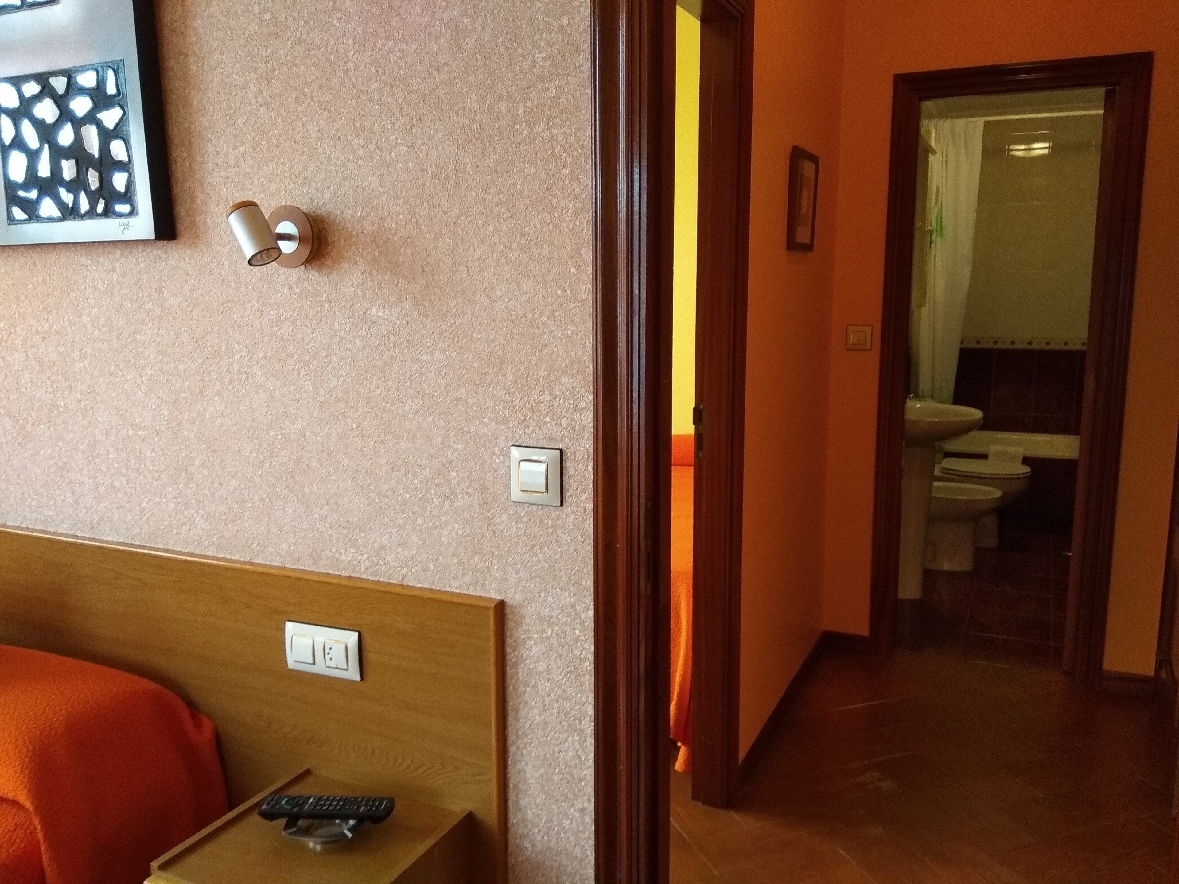 Hotelkamer met houten hoofdeinde, een afstandsbediening op een bijzettafeltje en een schilderij aan de muur.