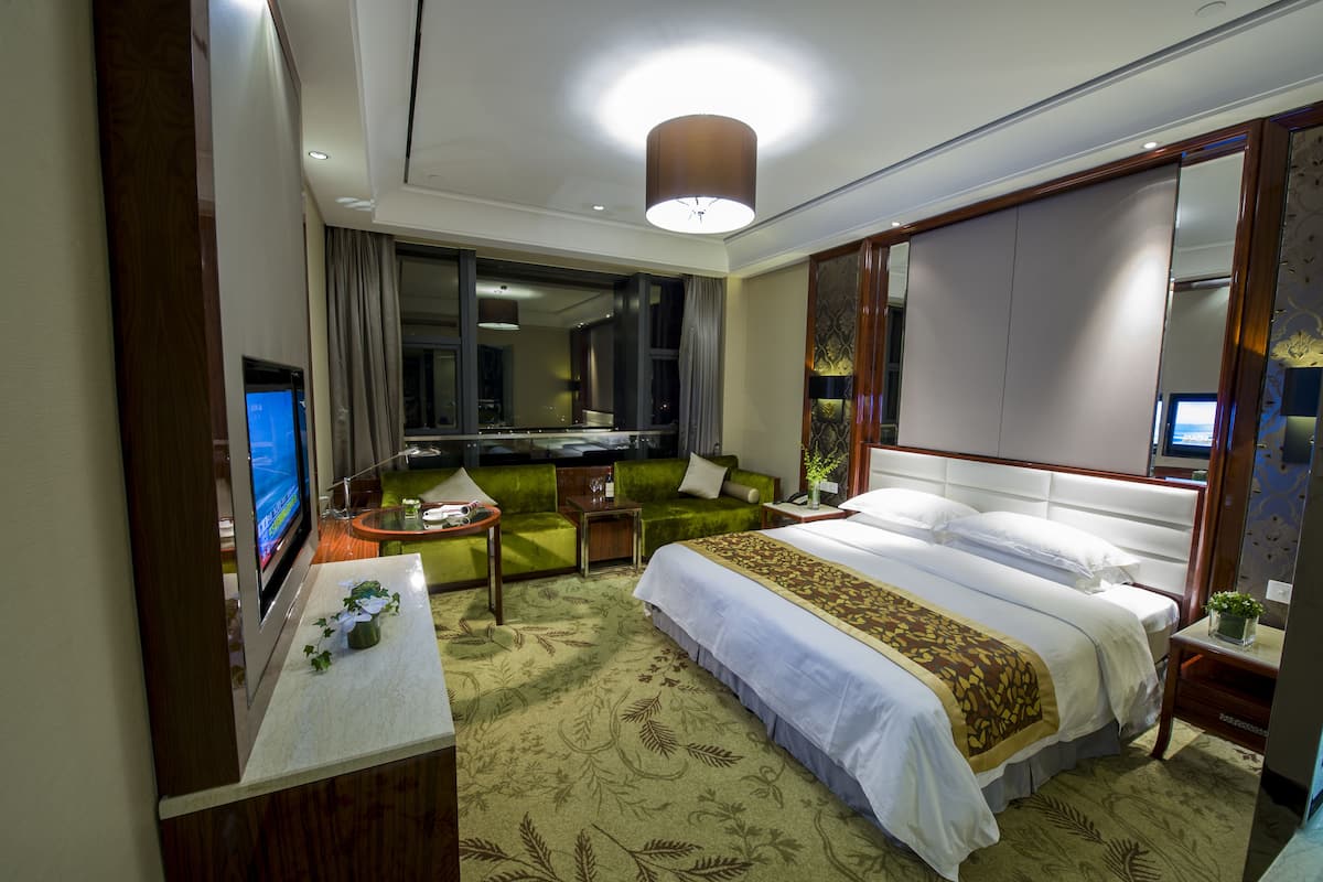 Ein Hotelzimmer mit einem großen Bett, einem grünen Sofa, einem Fernseher und einem Schreibtisch mit einem Computer.