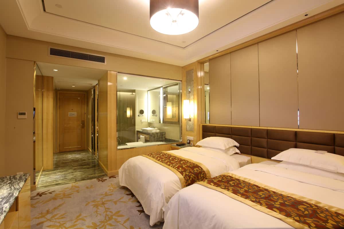 Ein Hotelzimmer mit zwei Betten, einem großen Spiegel und einem durchgegangenen Tür angedeuteten Badezimmer.