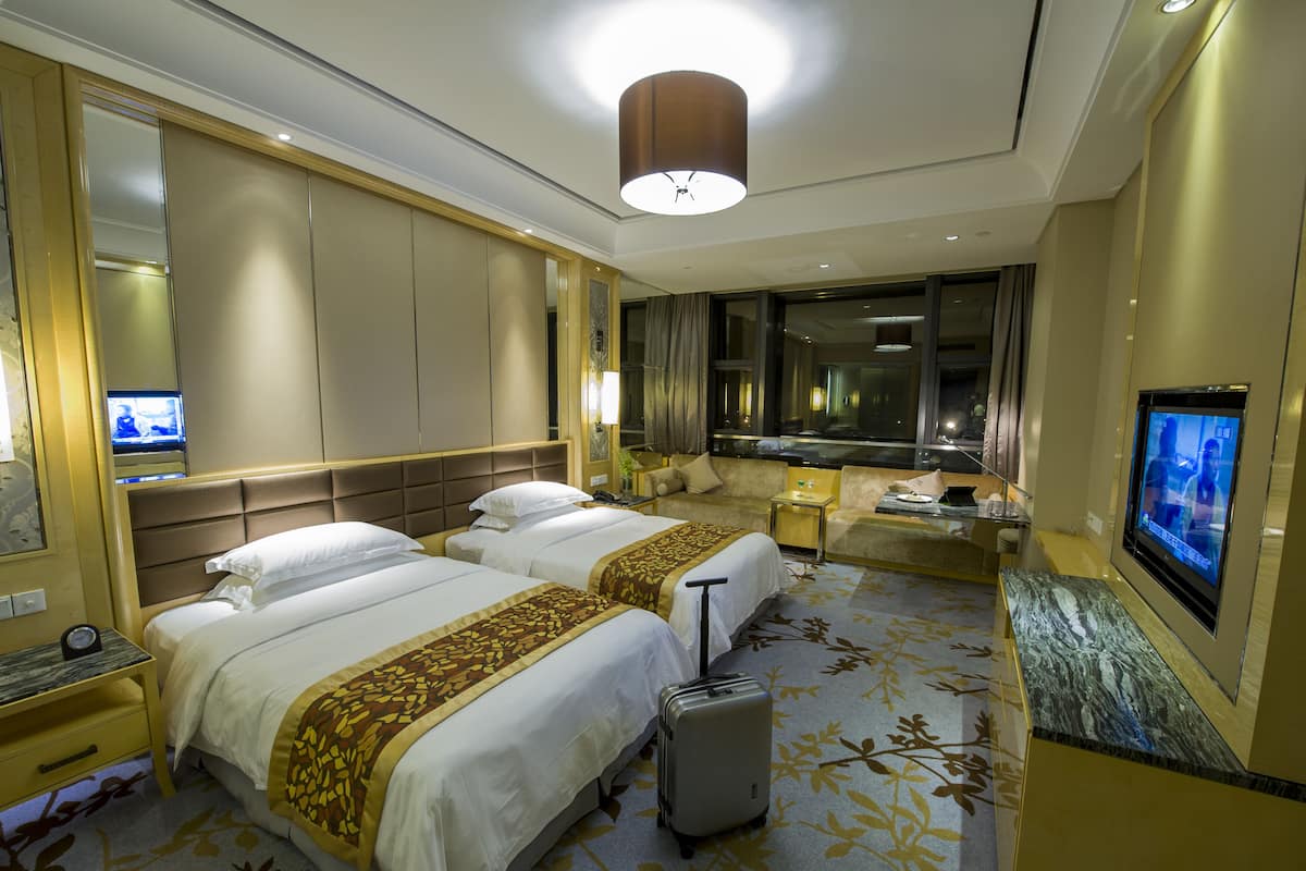 Ein Hotelzimmer mit zwei Betten, einem Schreibtisch, einem Fernseher und einem großen Fenster.