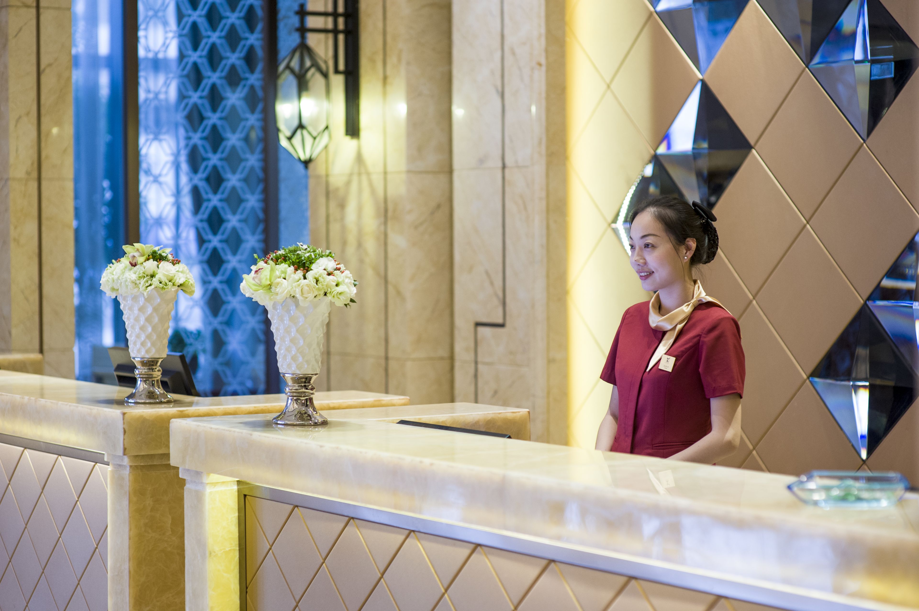 A reception desk with two vases of flowers, a marble counter, and a person standing behind it.