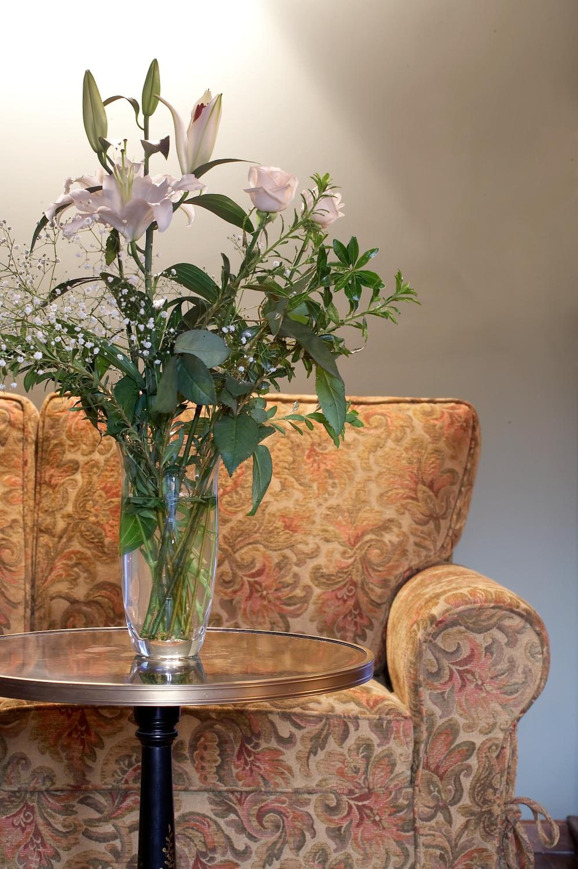 Un jarrón de cristal transparente con flores sobre una mesa redonda.