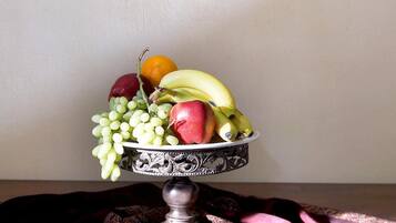 Un frutero sobre una mesa de madera, con un paño estampado debajo, frente a una pared decorada con cuadros.