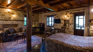 A rustic room with stone walls, wooden beams, a sofa, a bed, a table, and a television.