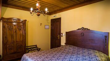 A bedroom with a wooden headboard, a patterned bedspread, a wooden wardrobe, and a chandelier.