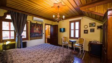 A room with a large bed, wooden ceiling, a chandelier, a television, and a small table with chairs.