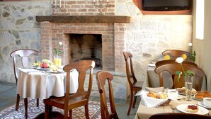 A dining area with a brick fireplace, wooden ceiling beams, and a television mounted above it.
