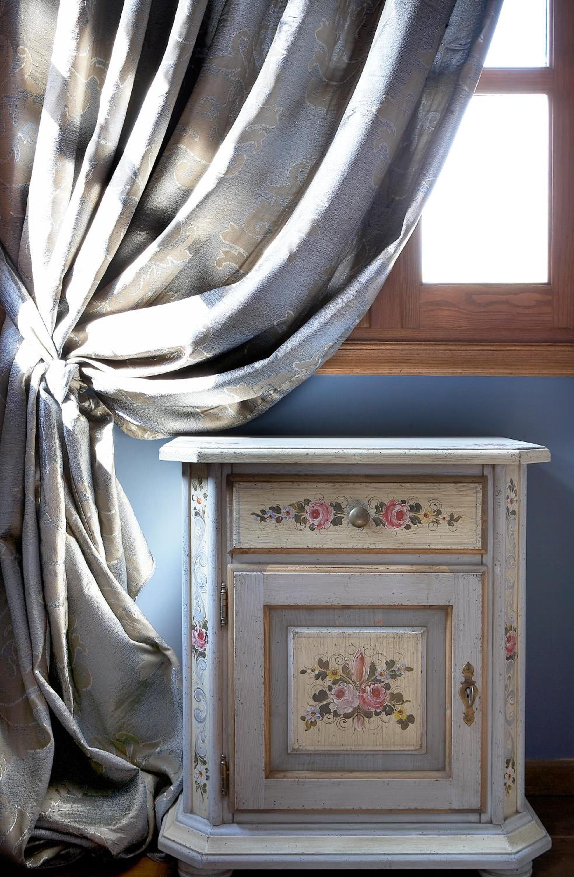 A vintage-style dresser with floral designs and a window with a wooden frame.