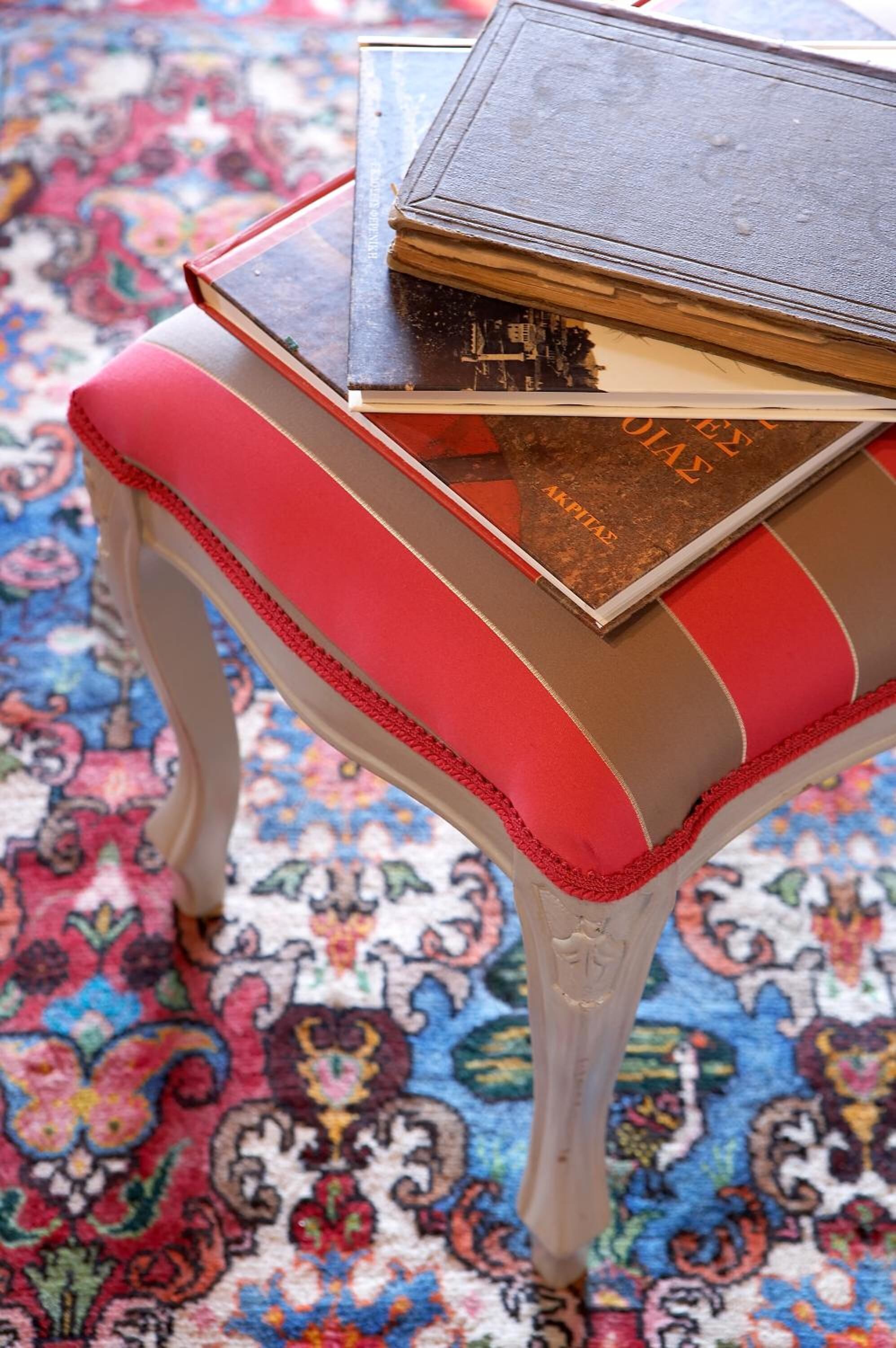 Una pequeña mesa ornamentada con un banco acolchado en tonos rojo y marrón, llena de libros.
