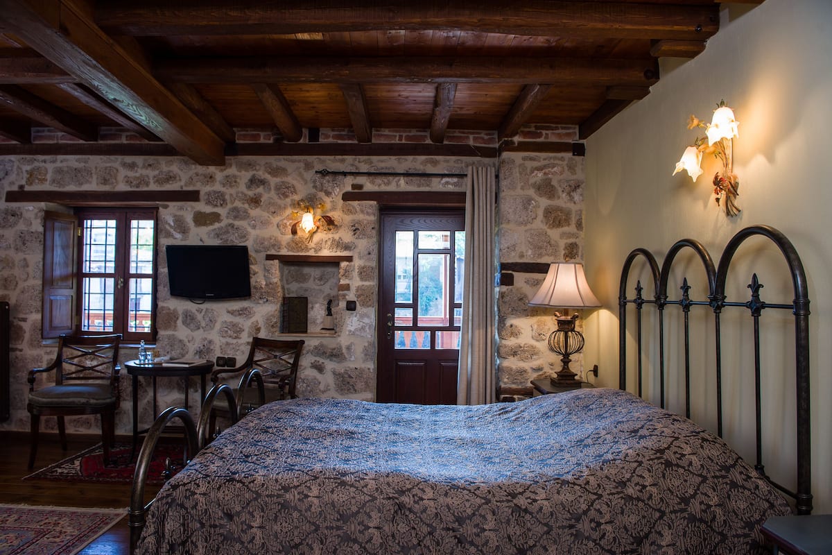 Una camera rustica con un letto, travi in legno, pareti in pietra, una televisione e una lampada.
