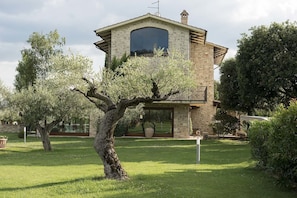 A stone building with a large window and a balcony, surrounded by well-maintained grass and trees.