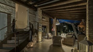 A spacious living area with a stone wall, a staircase, wicker furniture, and a large window. - Tenuta San Masseo (Assisi)