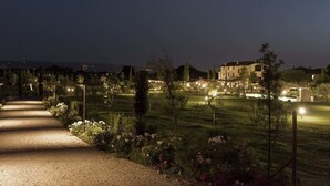 A nighttime view of a well-lit garden with a gravel path leading to a building. - Tenuta San Masseo (Assisi)