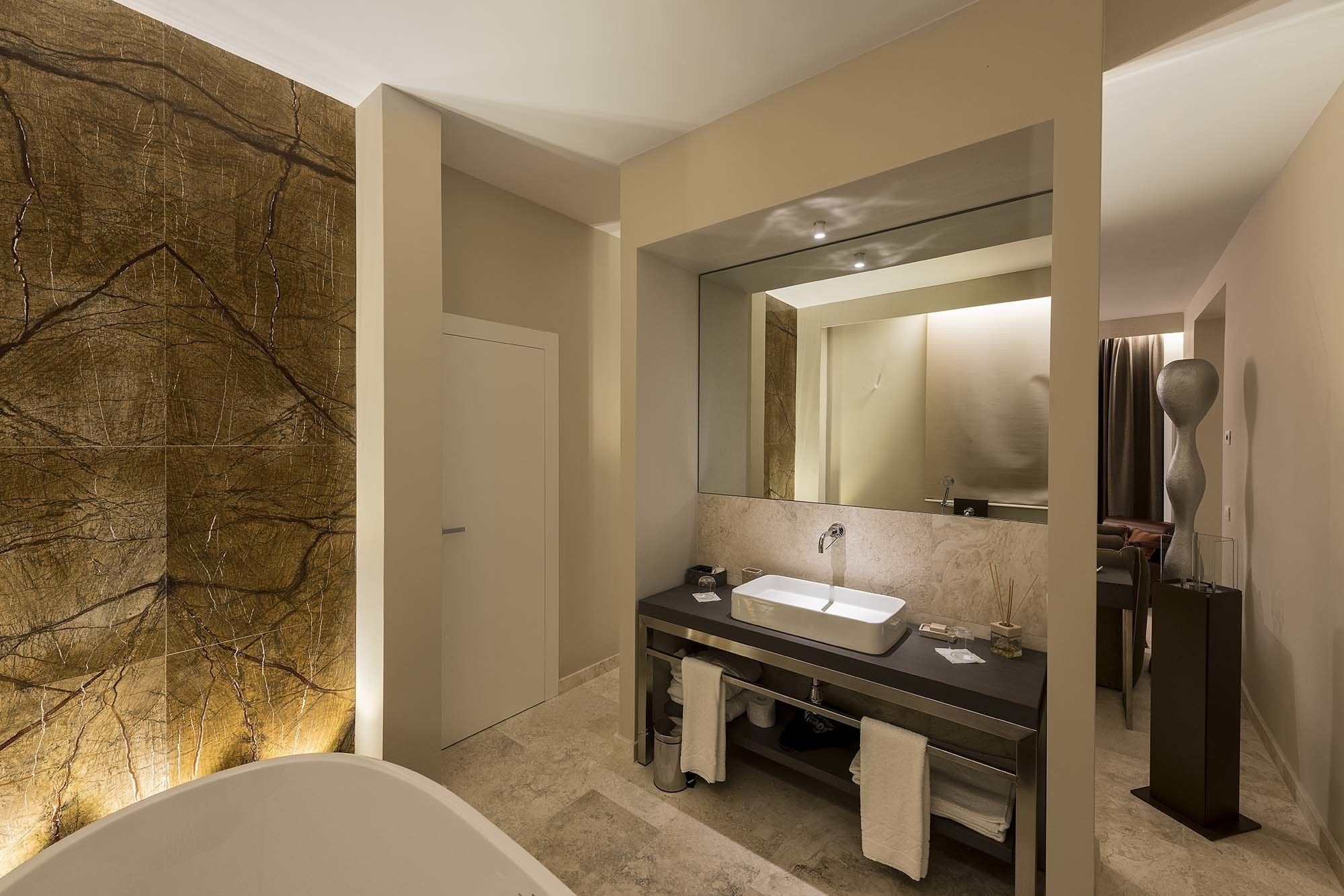 Ein modernes Badezimmer mit einer freistehenden Badewanne, einem großen Spiegel und einer Steinwand.