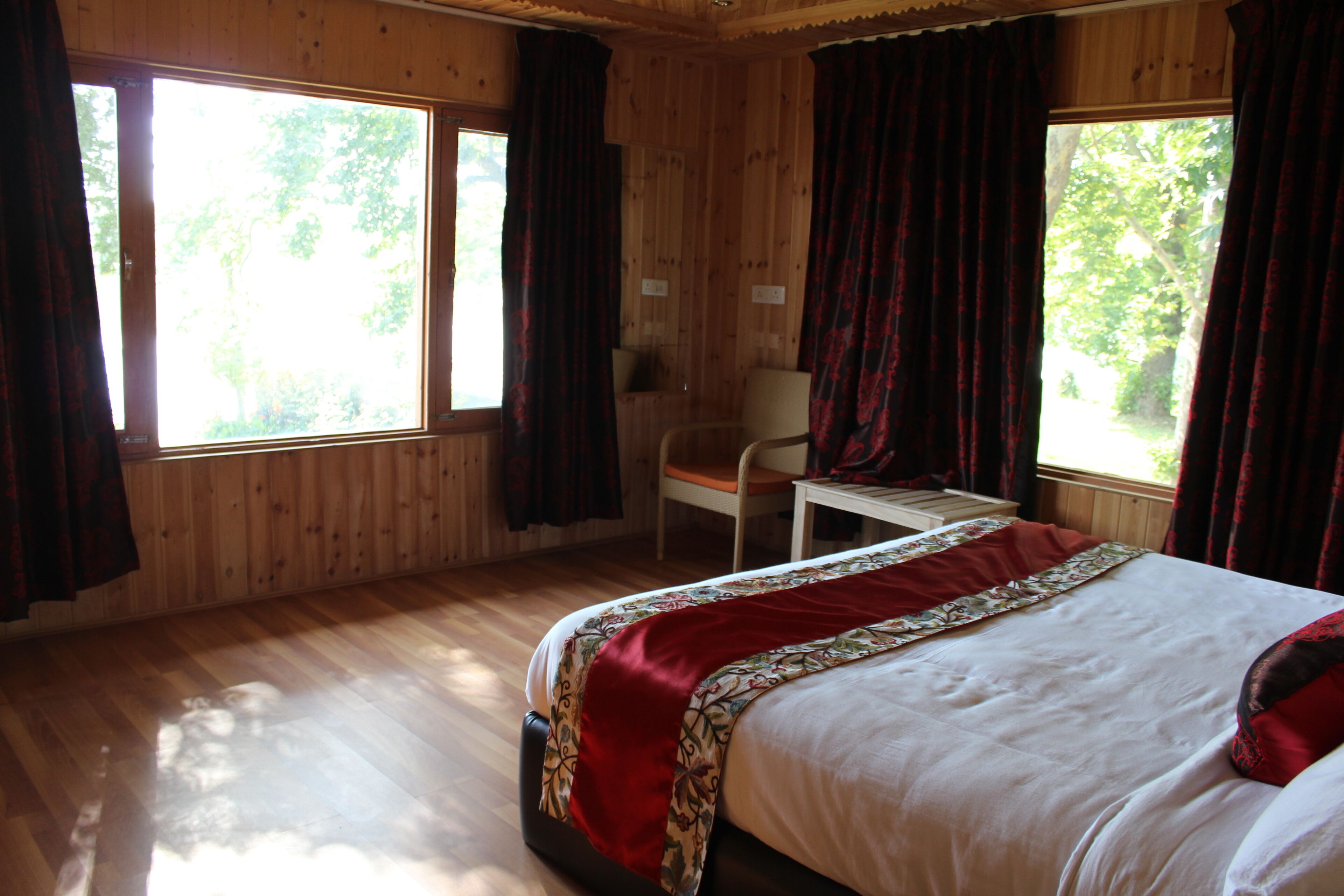 A wooden cabin room with a bed, a desk, and two windows with curtains.