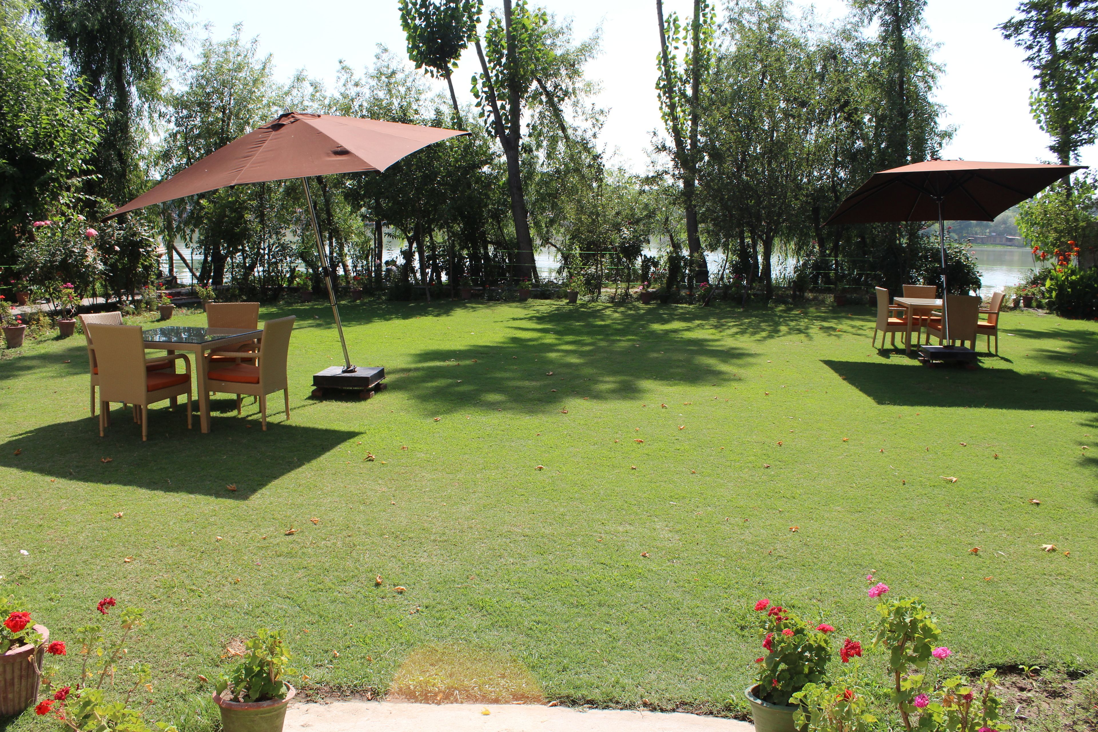 An outdoor patio area with a table and chairs under a large umbrella, surrounded by potted plants and a view of a lake.