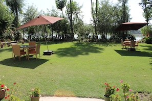 An outdoor patio area with a table and chairs under a large umbrella, surrounded by potted plants and a view of a lake. - Nigeen Lake View Resort (Srinagar)
