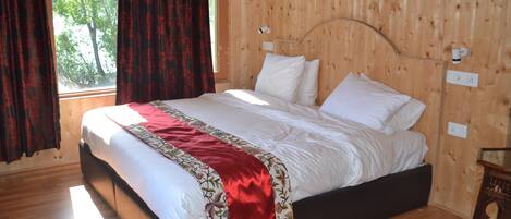 Um quarto com painéis de madeira, uma cama grande, uma janela com cortinas e uma mesa de cabeceira.