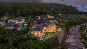 An aerial view of a resort with multiple villas, a swimming pool, and a view of the ocean and mountains. - Villa Gumamela Bali (Manggis)