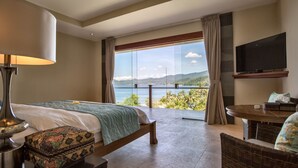 A hotel room with a bed, a table, a chair, a TV, and a view of the sea. - Villa Gumamela Bali (Manggis)