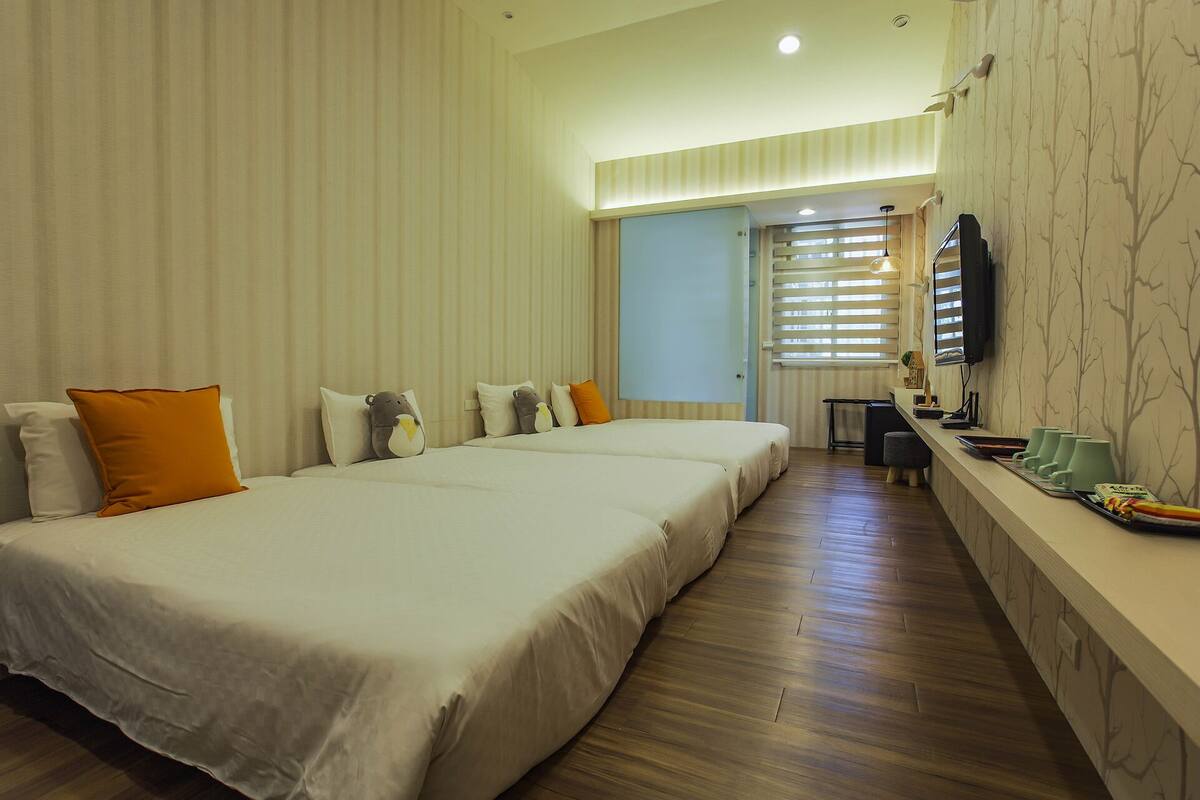 Quarto de hotel com duas camas, uma mesa de trabalho e uma televisão.