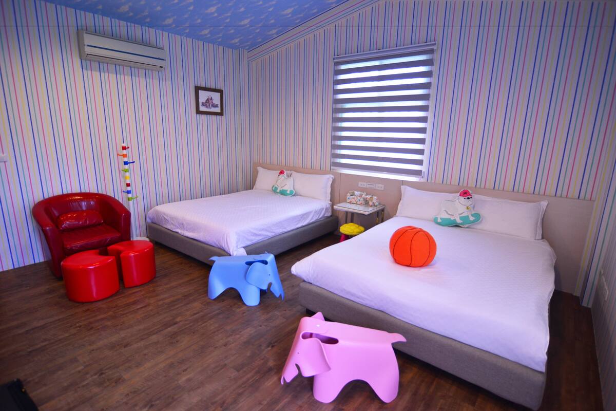 Quarto com papel de parede listrado, duas camas, uma cadeira vermelha e brinquedos de criança.