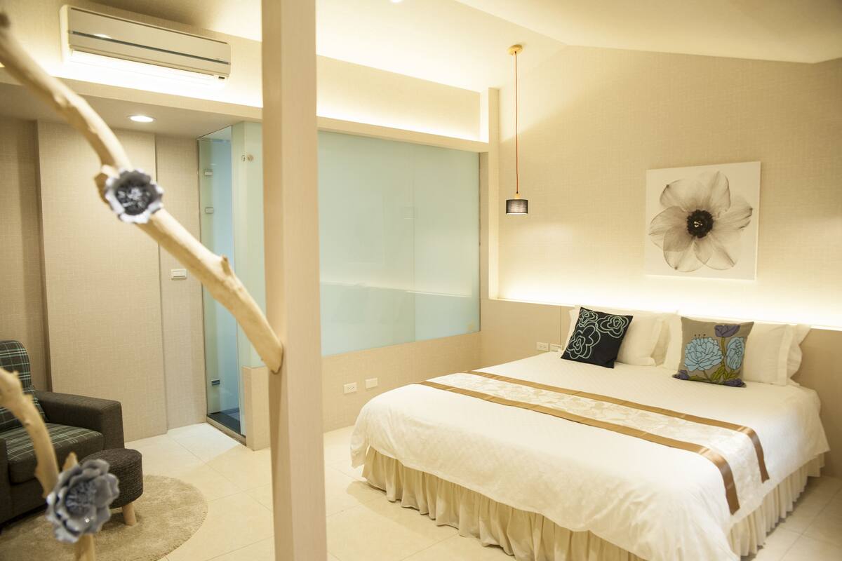 Quarto com uma cama grande, uma mesa de cabeceira, uma cadeira e uma obra de arte na parede.
