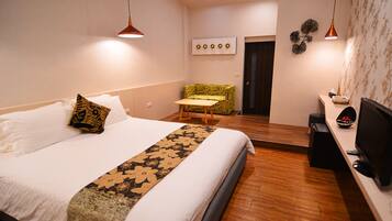 A hotel room with a bed, a small table, a TV, and a seating area with a patterned chair.