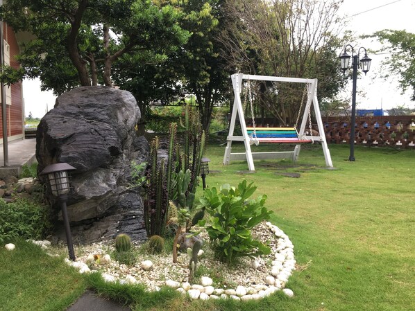 Un jardín con una roca, cactus y un columpio.