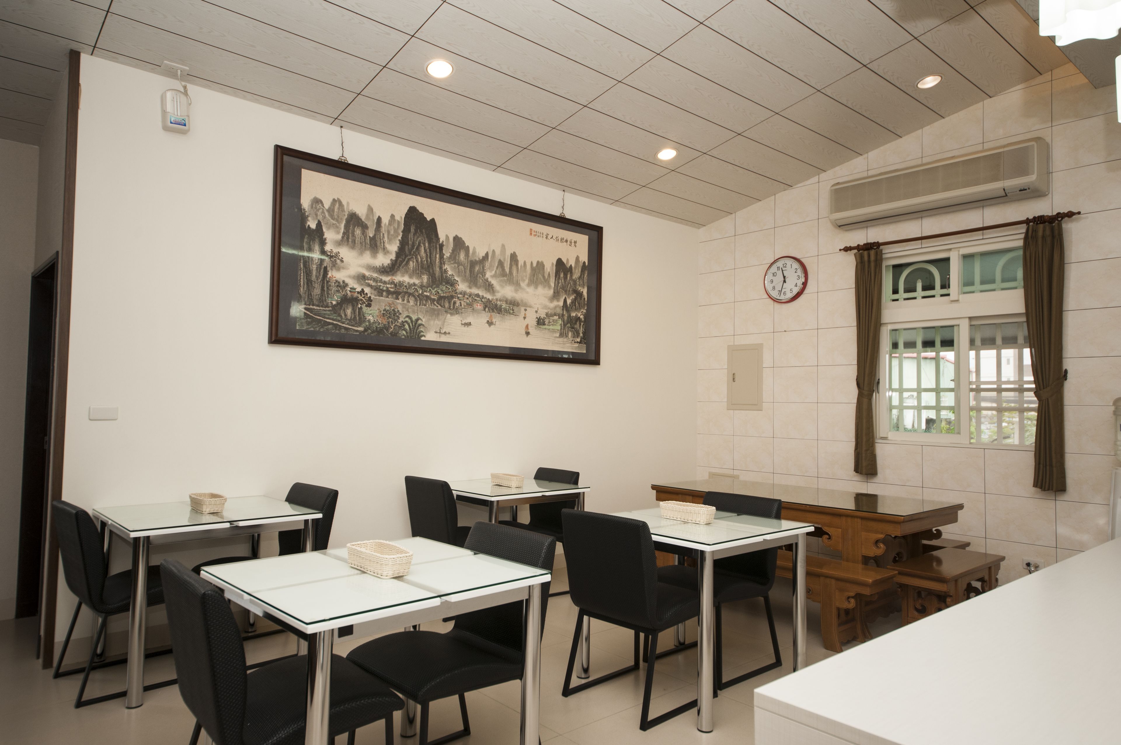 Un comedor con mesas y sillas, un reloj en la pared y un cuadro enmarcado.