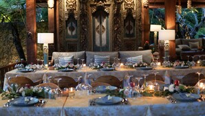 Una mesa de comedor elegantemente dispuesta, con centros de mesa florales, velas y un fondo de decoraciones ornamentales en la pared.