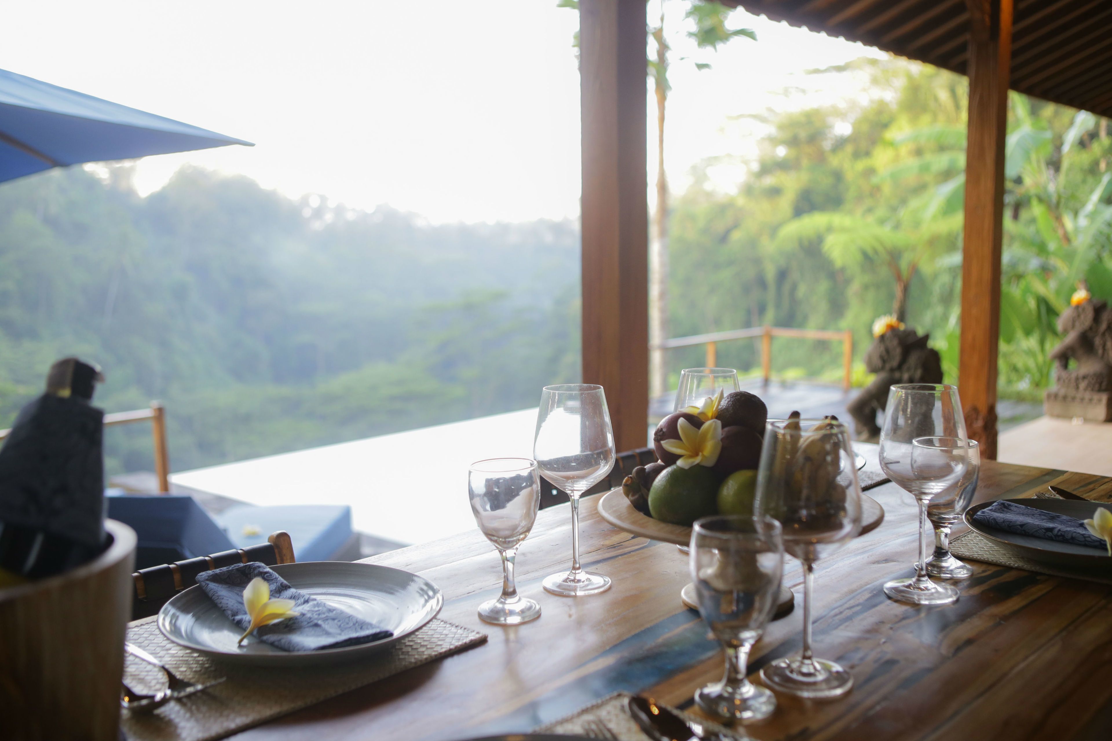 Mesa de jantar posta com taças de vinho, pratos e uma cesta de frutas.