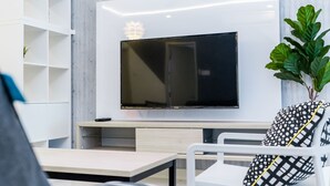 Un soggiorno moderno con una TV a schermo piatto montata a parete, un tavolino in legno, un divano bianco con cuscini decorati e una pianta in vaso.