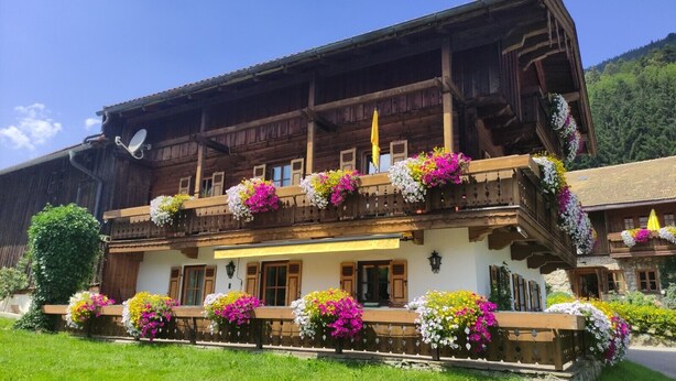 A traditional wooden chalet with balconies adorned with colorful flowers, a well-maintained garden, and a clear view of the surrounding landscape. - Alpenpanorama Vacation Rental, 68 square meters, with balcony, kitchen, Wi-Fi (Ruhpolding)