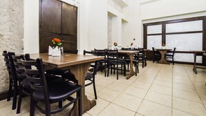 A dining area with wooden tables and chairs, a large window with frosted glass, and a decorative vase with flowers on one table.