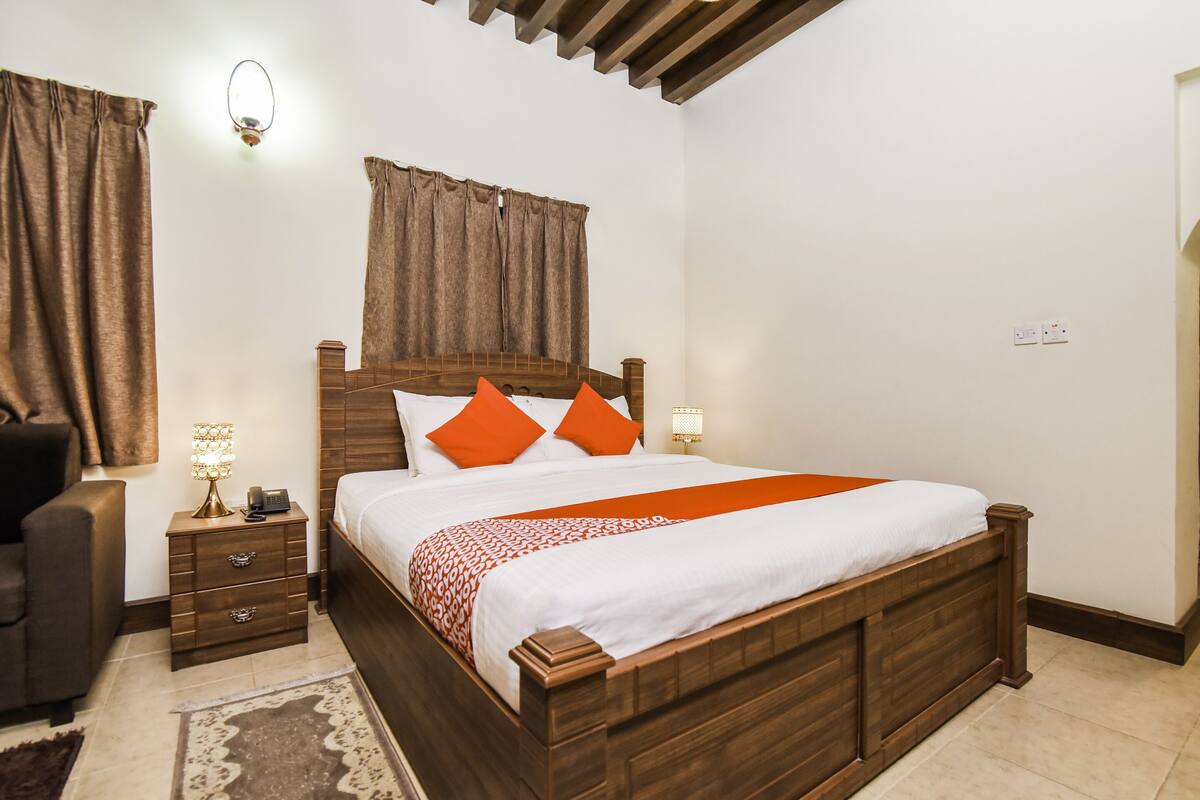 A bedroom with a wooden bed, two bedside tables, a nightstand, a lamp, and a chair.