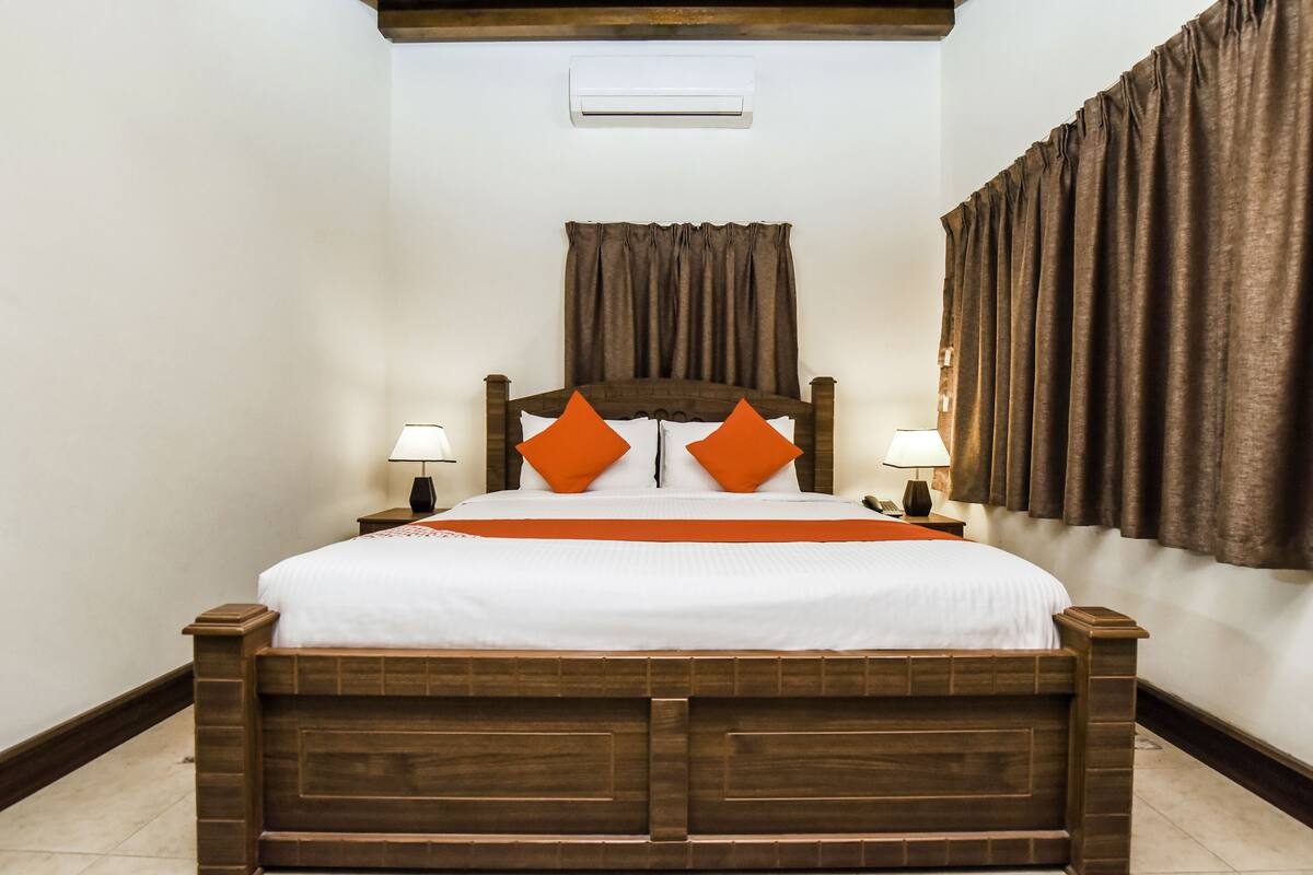 A wooden bed with a headboard, two bedside lamps, and orange pillows.