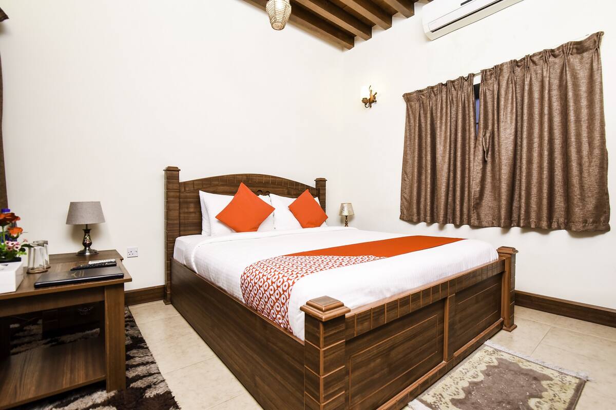 A neatly arranged bedroom with a wooden bed, a nightstand, a lamp, and a window with curtains.