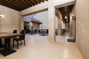 A spacious indoor area with a long table and chairs, a kitchen area in the background, and a tiled floor. -  Capital O160 Lumbini Dream Garden Guest House LLC (Dubai)