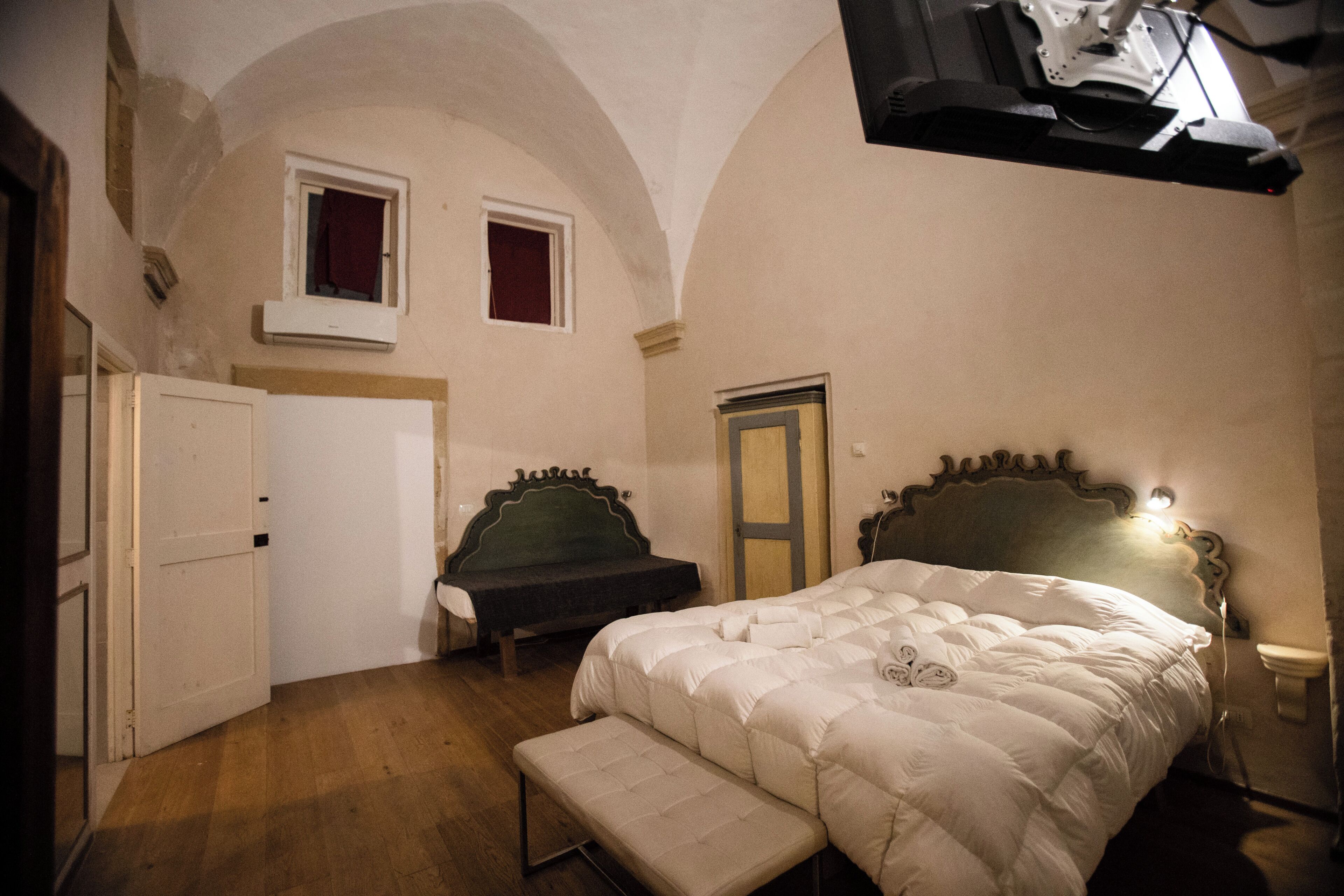 A bedroom with a large bed, a bench, a wardrobe, and a door.