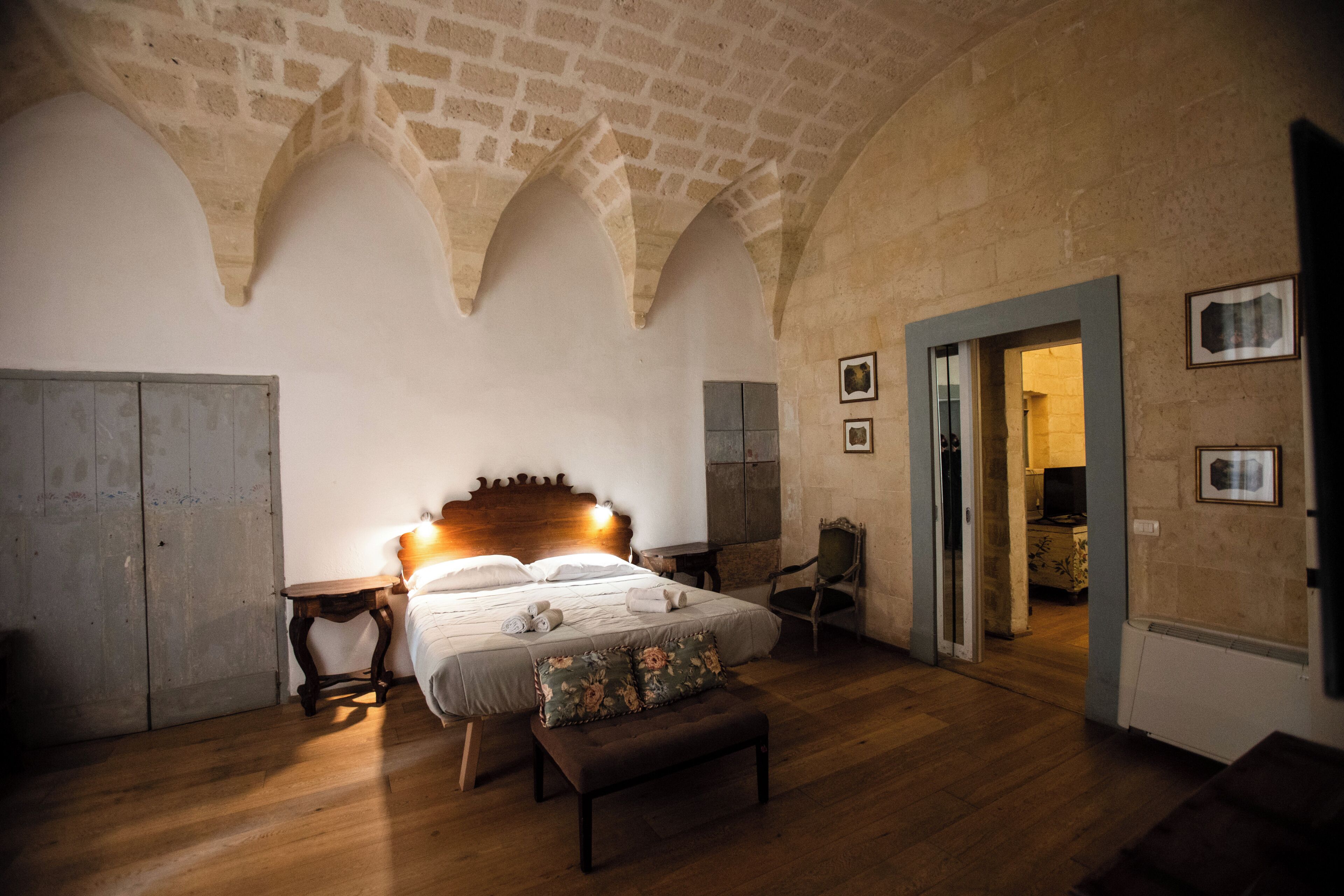 A bedroom with a wooden bed, a bench, a chair, and a door leading to another room.