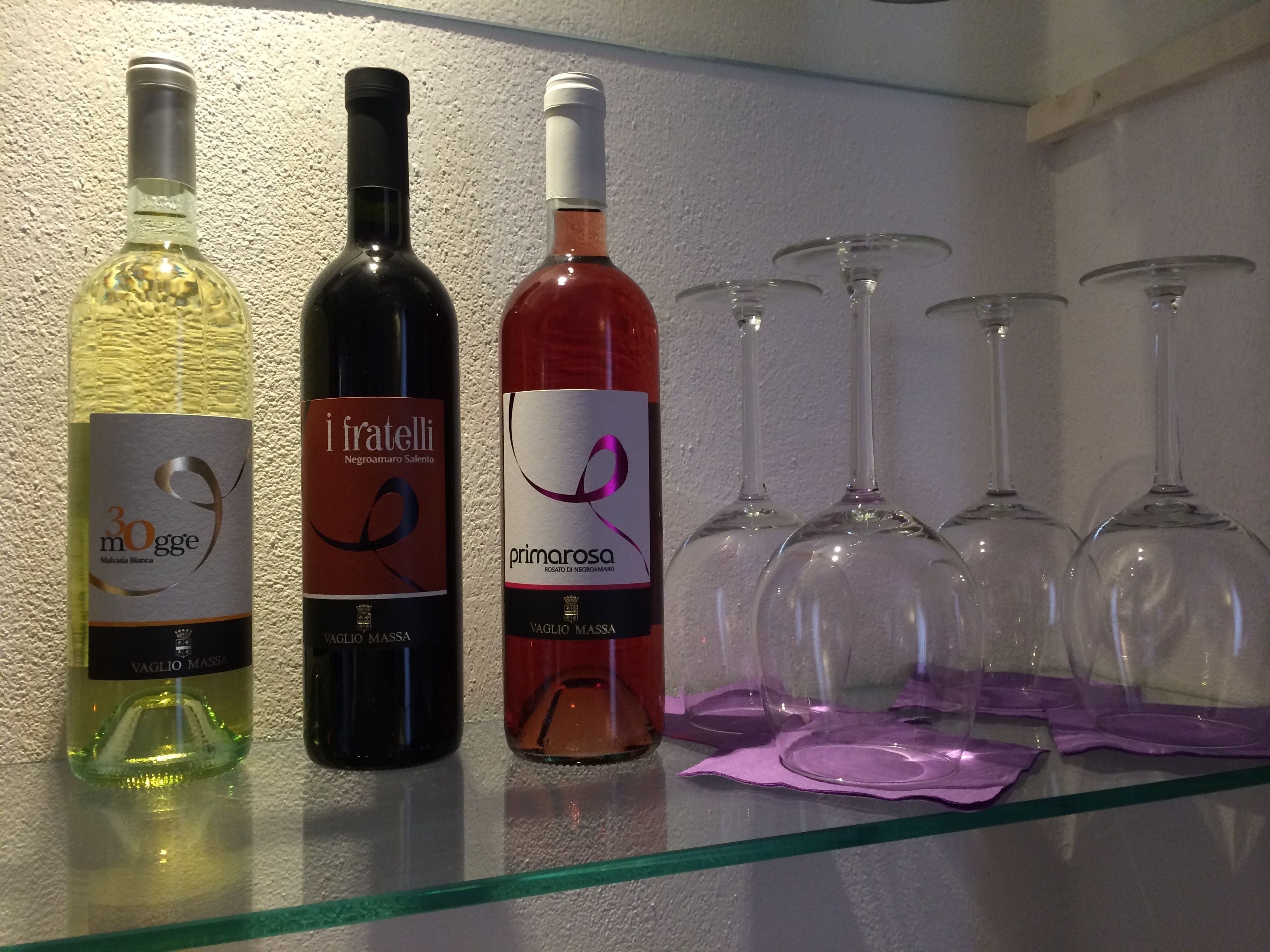 Three wine bottles and six wine glasses on a glass shelf.
