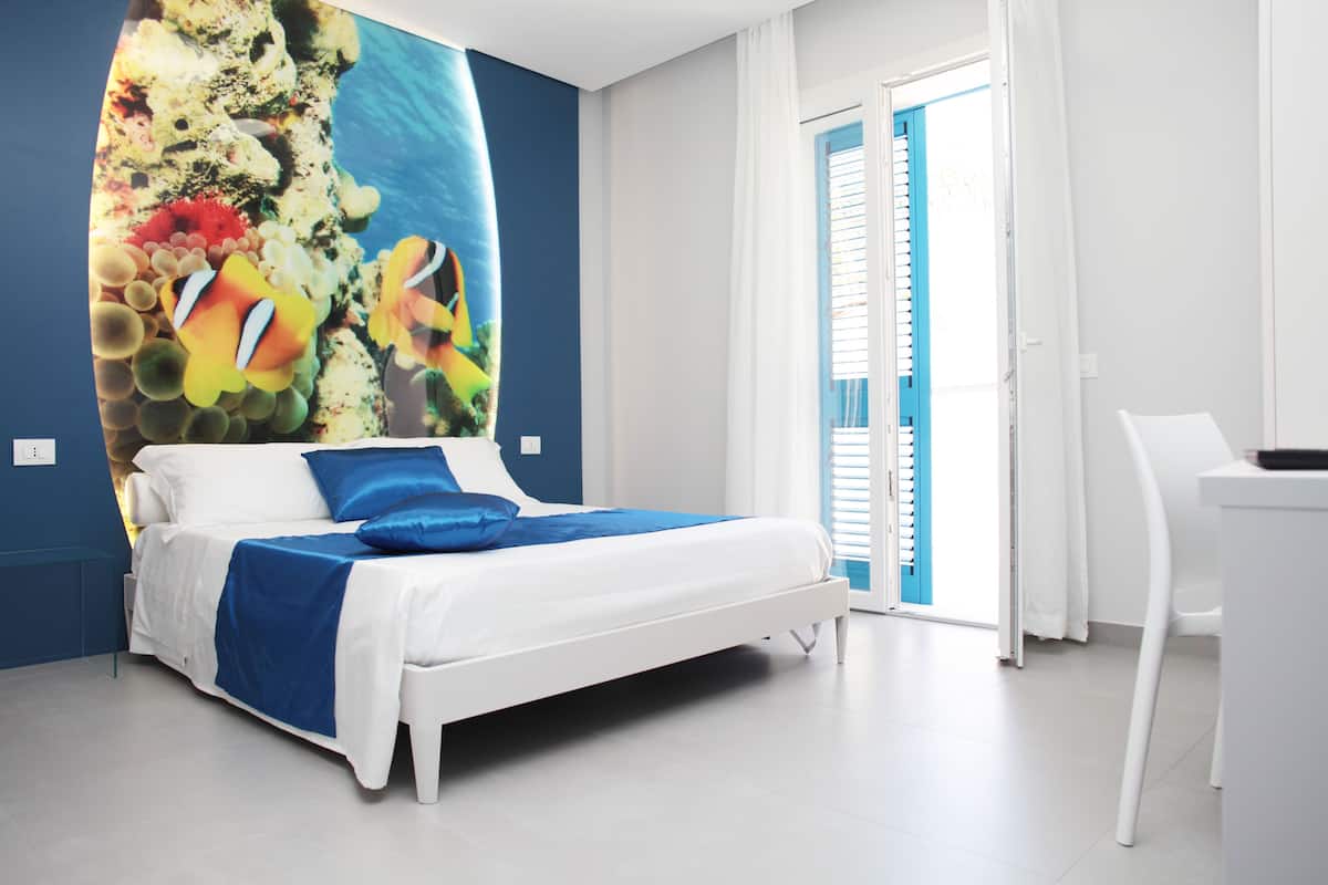 Une chambre moderne avec un lit, un bureau et une grande fresque représentant la vie marine sur le mur.