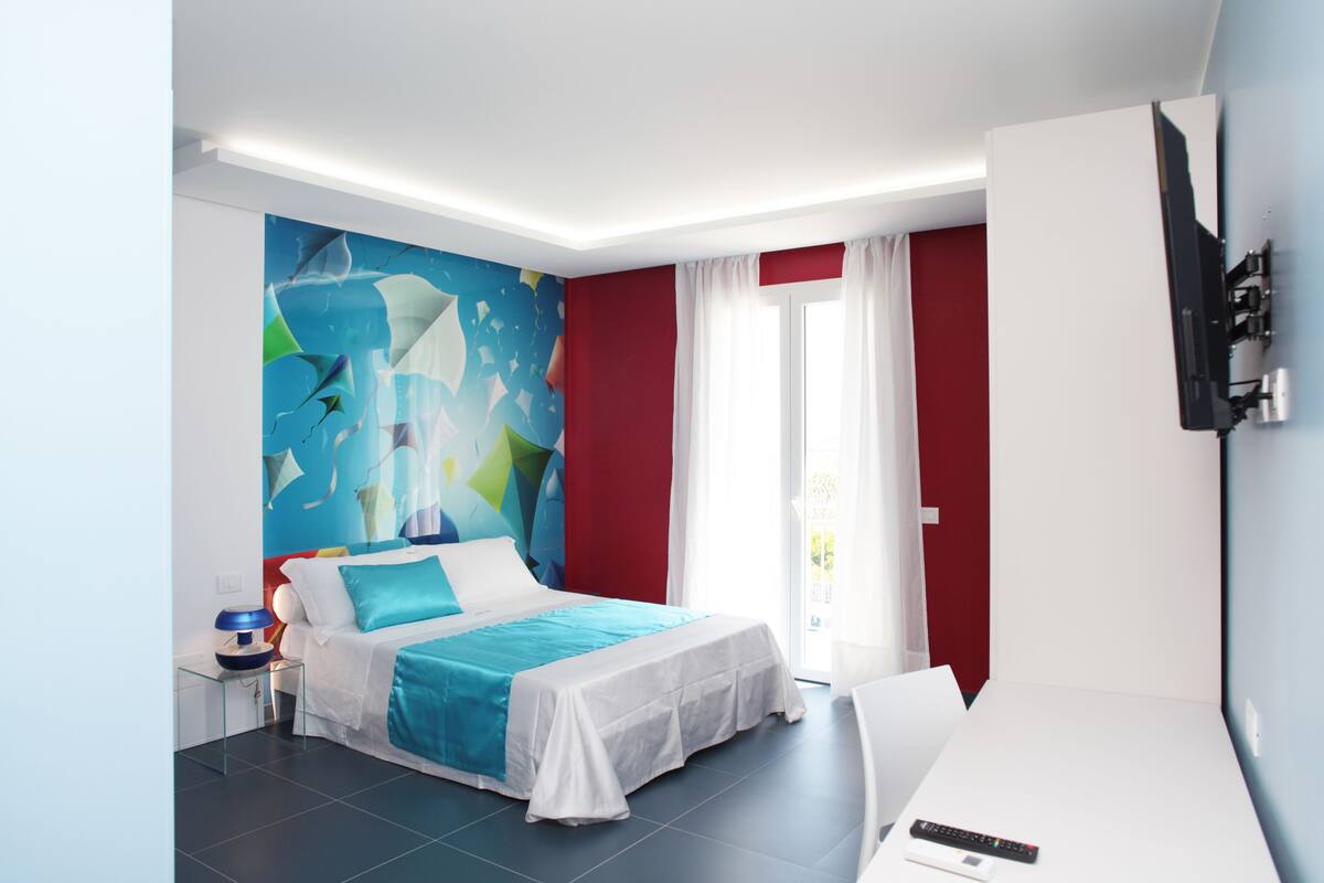 Une chambre d’hôtel moderne, équipée d’un lit, d’un téléviseur fixé au mur et d’une grande fenêtre avec des rideaux.