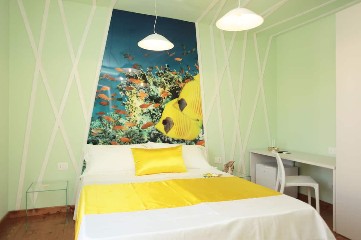 Une chambre comprenant un lit, un bureau et une fresque murale représentant un paysage sous-marin.